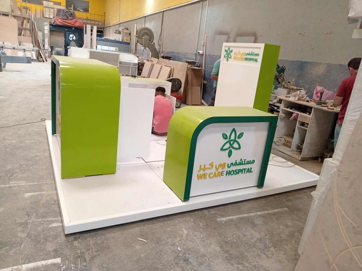 A reception unit mid-build on the workshop floor: a counter with curved edges and a face carrying built-up letters, the crew working behind it